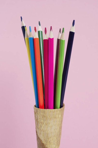 Nahaufnahme einiger Buntstifte in verschiedenen Farben in einem Eiskegel auf rosa Hintergrund - Foto, Bild