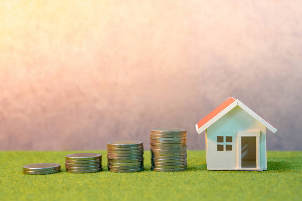 Real estate investment or Home mortgage loan rate. Property ladder concept. Coins stack, house model and table clock on green grass. Investment and business growth background - Photo, Image