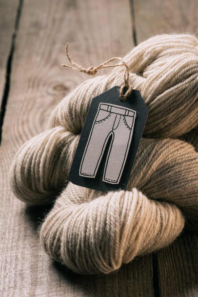 selective focus of beige yarn ball and tag with trousers on wooden background - Foto, Imagen