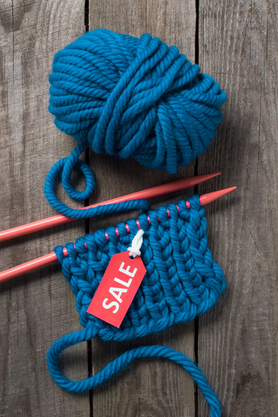 top view of blue knitting needles, blue yarn ball and sale tag on wooden background - Photo, Image