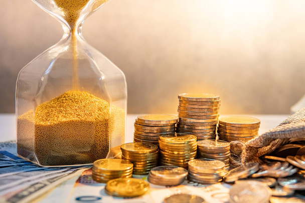 砂と国際通貨の紙幣とコイン スタック テーブルで砂時計の形を実行します。時間を投資。退職の節約。締め切りのビジネス コンセプトの緊急カウント ダウン タイマー - 写真・画像