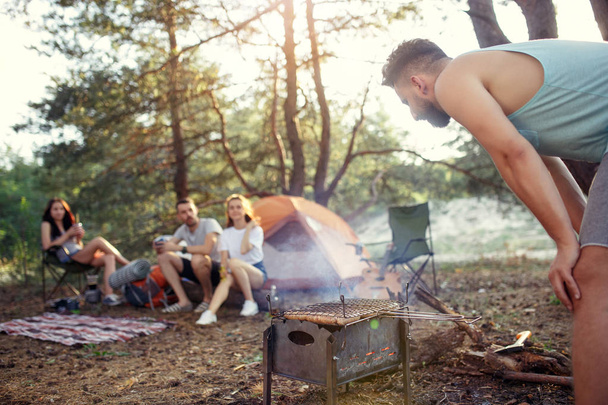 Party, camping of men and women group at forest. They relaxing, singing a song and cooking barbecue against green grass. The vacation, summer, adventure, lifestyle, picnic concept - Foto, Imagem