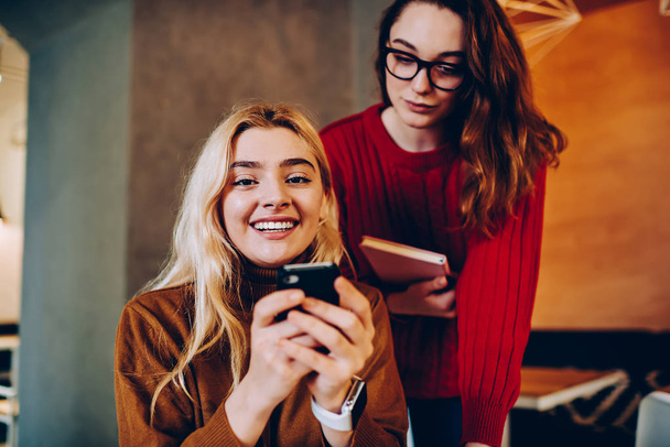 Cheerful hipster girls reading news about sales in web store on smartphone, happy teen girl showing mail with information about discounts to her friend can't wait for making booking on cellular - Фото, зображення