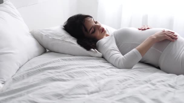 Schwangere schöne Frau liegt auf Bett und streichelt Babybauch - Filmmaterial, Video