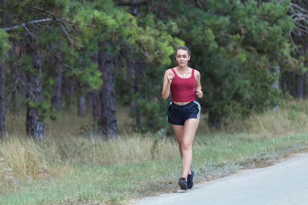 Young woman running outdoors on a beautiful day. Girl running on forest trail to loose weight and maintain a healthy life. - Photo, Image
