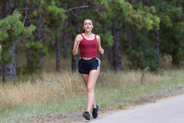 Young woman running outdoors in a city park on a beautiful day. Girl running on forest trail to loose weight and maintain a healthy life. - Fotoğraf, Görsel