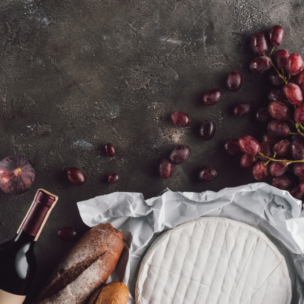 flat lay with food composition of bread loafs, camembert cheese and bottle of wine on dark surface - Photo, image