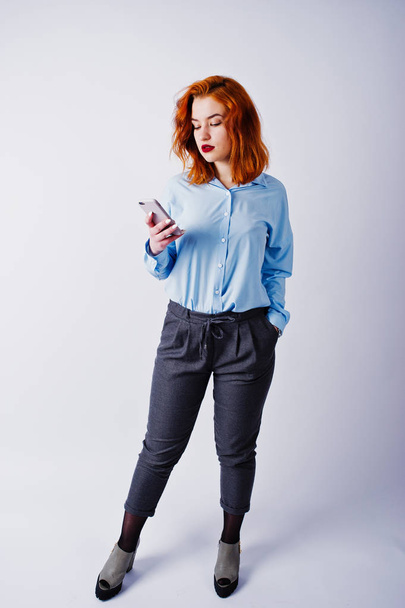 Portrait of a young redheaded businesswoman in blue shirt and trousers texting on the phone. - Фото, зображення