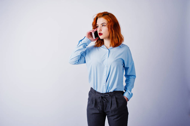 Portrait of a young redheaded businesswoman in blue shirt and trousers talking on the phone. - Valokuva, kuva