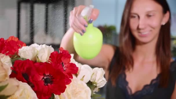 Young female florist spraying water on bunch of flowers in flower shop, close-up - Séquence, vidéo