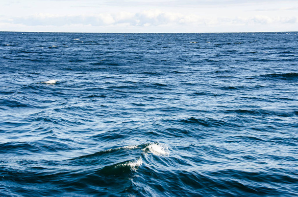 Κύματα στην επιφάνεια του νερού με συννεφιασμένο ουρανό. Βαθύ μπλε χρώμα - Φωτογραφία, εικόνα