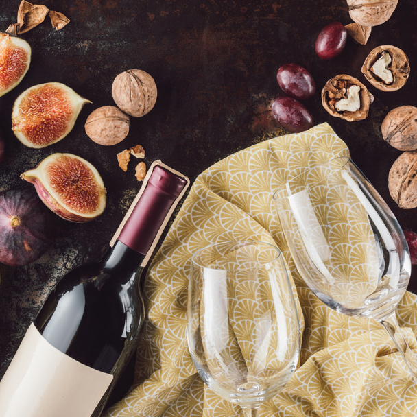 top view of bottle of wine, empty glasses, hazelnuts and figs on dark tabletop - 写真・画像