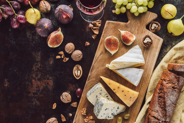 food composition with assorted cheese, glass of wine and fruits on dark tabletop - Photo, Image