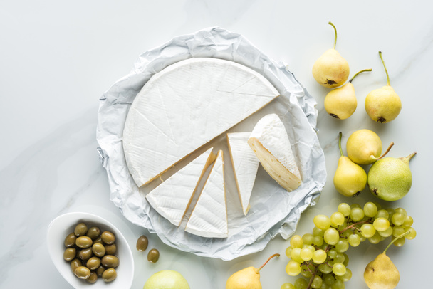 flat lay with camembert cheese, olives and fruits on white marble surface - Photo, Image