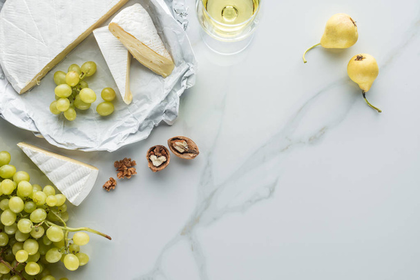flat lay with glass of wine, camembert cheese, pears and grape on white marble surface - Fotografie, Obrázek