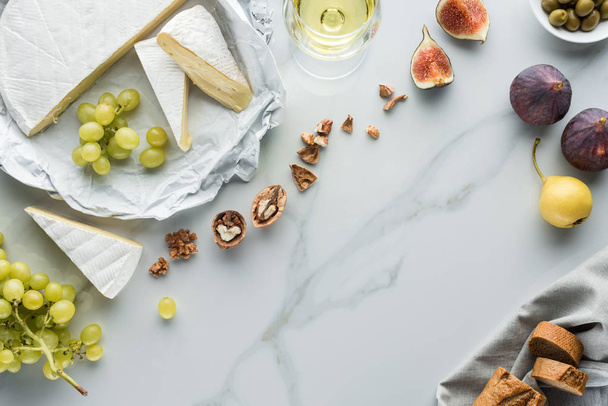 flat lay with cheese, wine and fruits arranged on white marble surface - Fotó, kép