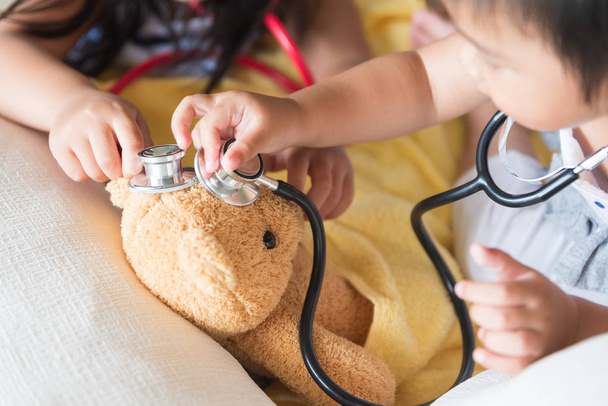 Sevimli küçük kız doktor stetoskop ve oyuncak ayı ile oynuyor. Çocuk ve sağlık kavramı. - Fotoğraf, Görsel