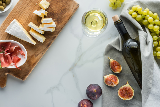 flat lay with wine, camembert cheese, jamon, figs and grape on white marble tabletop - 写真・画像