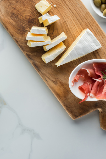 flat lay with camembert cheese and jamon on wooden cutting board on white marble tabletop - Photo, Image