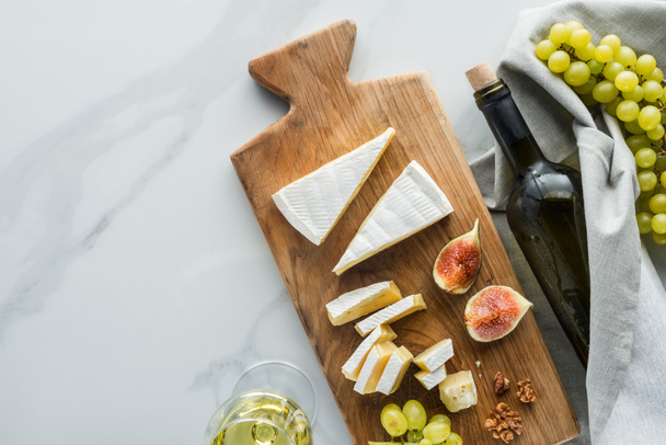 flat lay with food composition of camembert cheese on cutting board, wine and fruits on white marble surface - 写真・画像