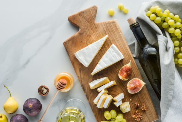plano con la composición de los alimentos de queso en la tabla de cortar, miel, vino y frutas en la superficie de mármol blanco
 - Foto, Imagen