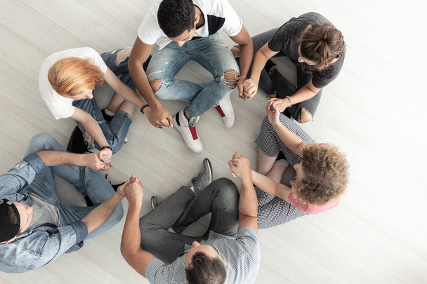 Vista superior de los adolescentes sentados en círculo y tomados de la mano durante la terapia de grupo
 - Foto, Imagen