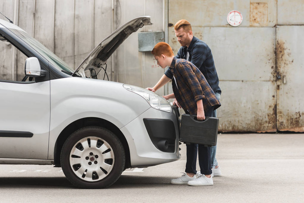 side view of father and son repairing car with open hood together - Valokuva, kuva