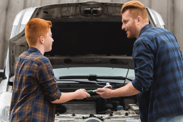 preteen son giving tool for repairing car to father - Photo, Image