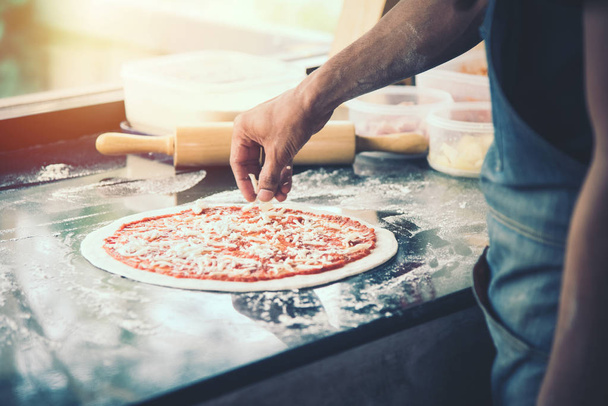 hand Chef preparing spread cheese on pizza on marble table, closeup making pizza - Foto, imagen