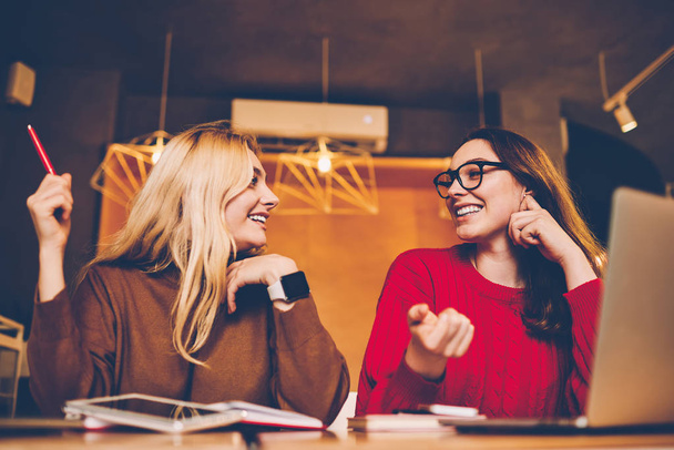 Happy young women communicating about successful freelance business working together remotely in cafe, cheerful hipster girls enjoying friendly talk joking with each other while doing homewor - Фото, изображение