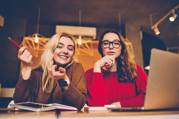 Portrait of cheerful hipster girls enjoying learning in coworking office completing homework easily together, smiling creative female students looking at camera satisfied with learning process - Photo, Image