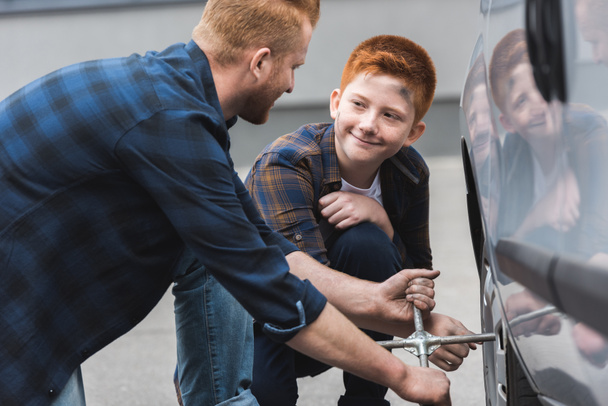 ginger hair father and son changing tire in car with wheel wrench  - Photo, Image