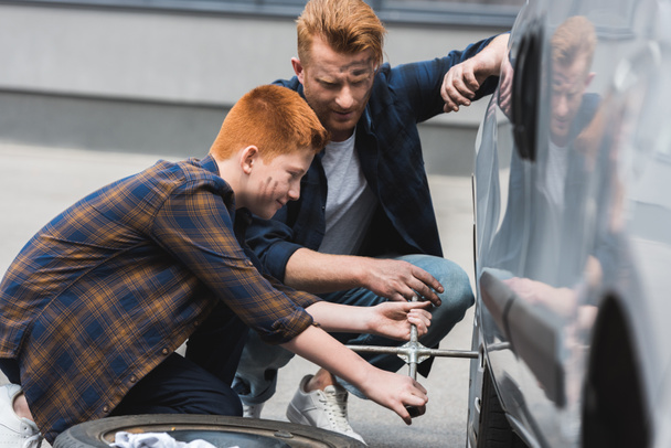 side view of father and son changing tire in car with wheel wrench - Φωτογραφία, εικόνα