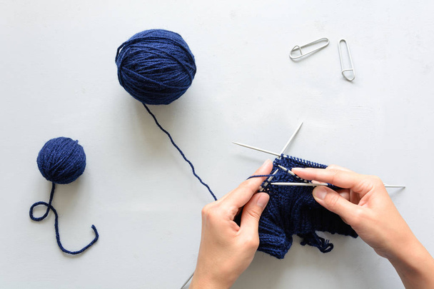 Girl knits blue hat knitting needles on gray wooden background. Process of knitting. Top view. Flat lay - Φωτογραφία, εικόνα
