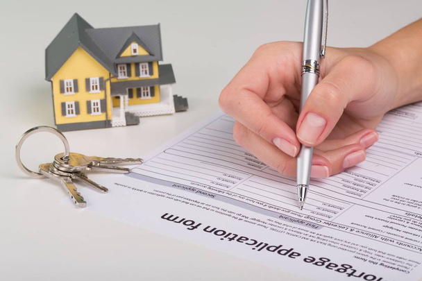 Contrato de préstamo inmobiliario, documento de firma de mano femenina, llaves de la casa en la mesa
 - Foto, Imagen