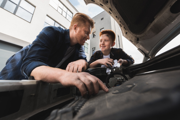 Vater und Sohn reparieren Auto und schauen einander an - Foto, Bild