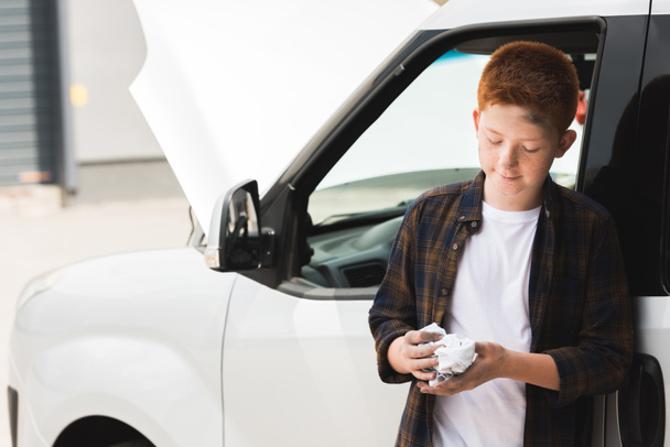 red hair preteen boy repairing car and holding napkin - Foto, afbeelding