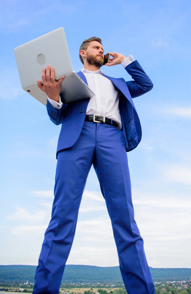 Always in touch. Communicating skill. Man well groomed businessman holds laptop while speak phone blue sky background. Guy formal suit modern technology manager entrepreneur answer phone call - Fotoğraf, Görsel