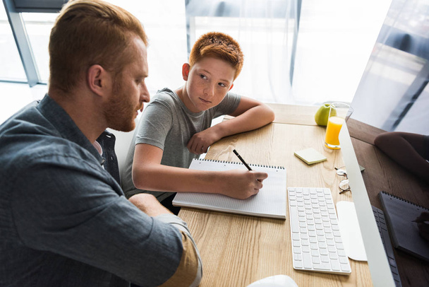 side view of father helping son doing homework at home - Photo, Image