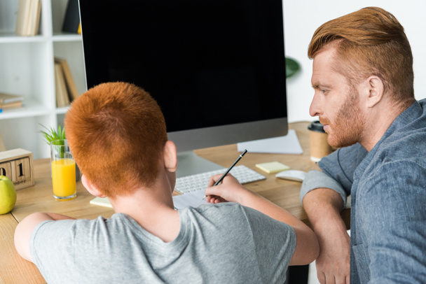 father helping ginger hair son doing homework at home - 写真・画像