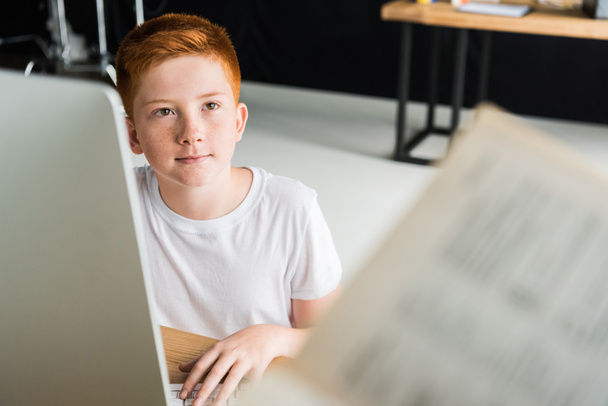 boy sitting at table with computer and looking away at home - Foto, Bild