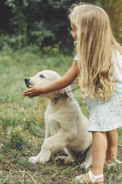 kleines süßes blondes Mädchen spielt mit ihrem Welpen Golden Retriever. - Foto, Bild