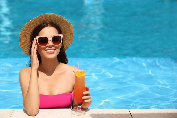 Beautiful young woman with cocktail in blue swimming pool - Foto, Imagem
