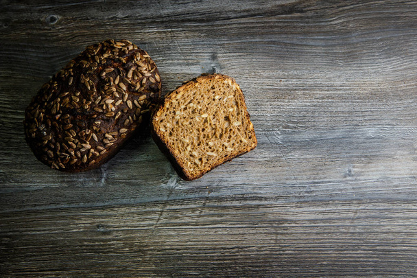 whole and half of handmade delicious handmade rectangular rye bread with sunflower seeds on dark table background - Fotó, kép