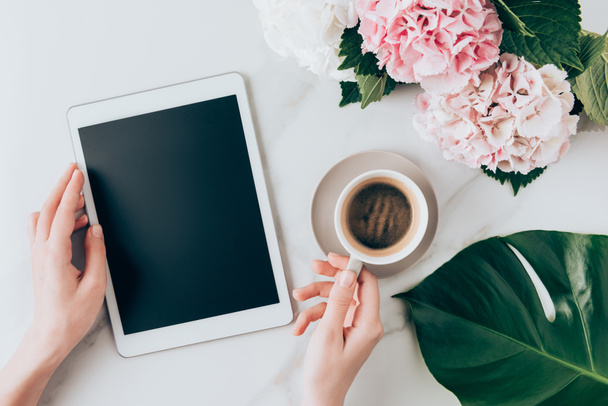 Kadın el ile kahve fincanı ve dijital tablet ile boş ekran görünümünü HORTENSIA çiçekli masa üzerinde kırpılmış  - Fotoğraf, Görsel