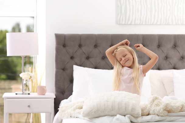 Cute little girl stretching in bed with pillows at home - Foto, Imagem