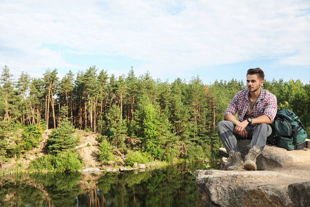 Young man on rock near lake and forest. Camping season - Foto, imagen