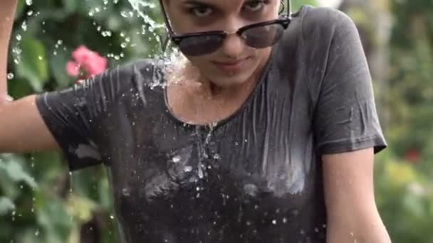 Jeune jolie fille percée dans les lunettes de soleil s'amuser avec pulvérisation d'eau de tuyau dans le jardin. T-shirt de loisirs d'été et humide. Beau corps
 - Séquence, vidéo