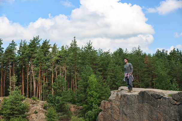 Young man on rock near beautiful forest. Camping season - Фото, изображение