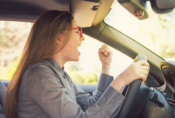 Side view of young woman in glasses driving car and gesturing emotionally in anger looking away during rush hour - Foto, Imagen